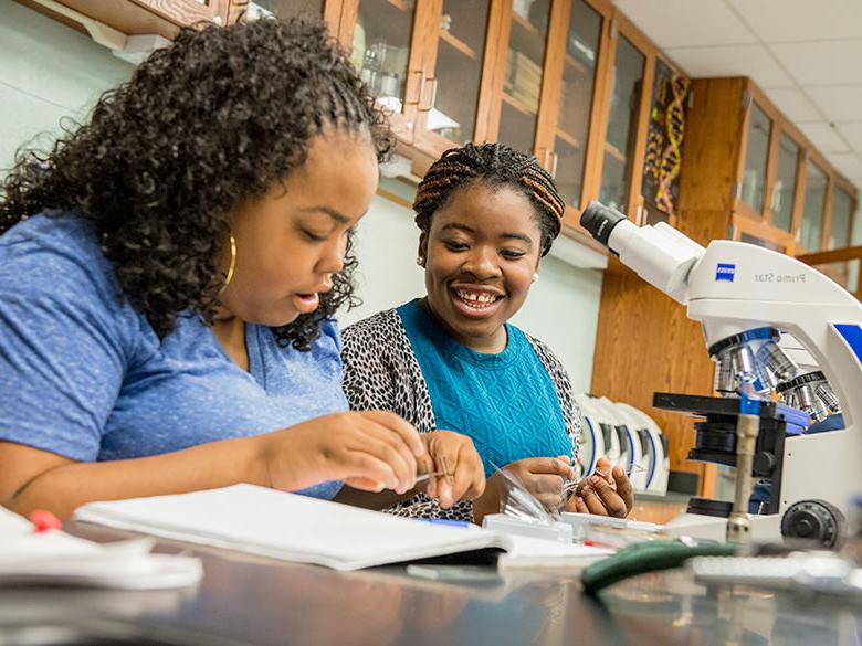 Two female students seated before a microscope in a biology class